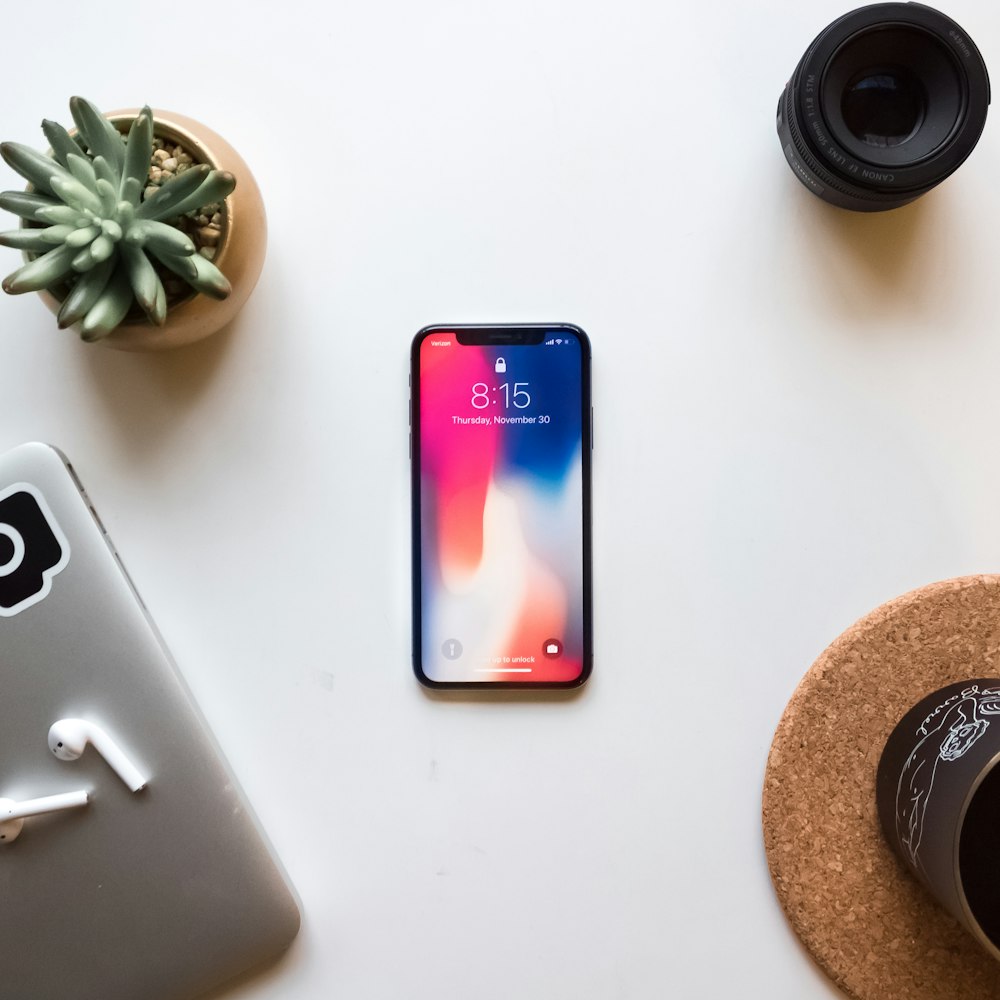 Celular, auriculares y lente de cámara sobre un escritorio blanco